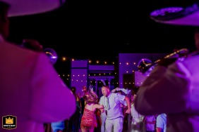 A joyful couple in Tulum link arms and swing each other in a lively circle on the dance floor, surrounded by festive lighting and laughter, their expressions filled with happiness and celebration.